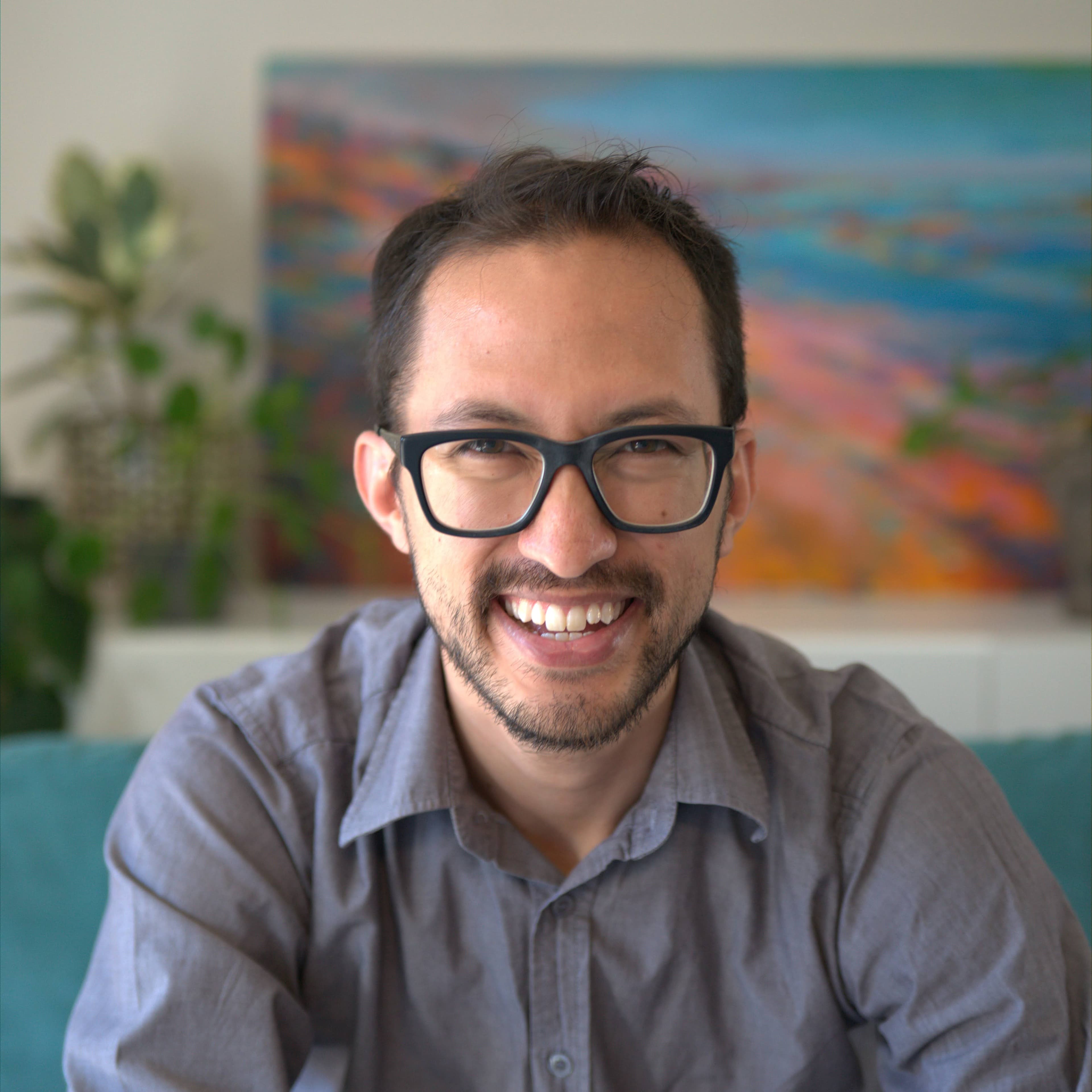 Daniel Nash smiling in a close-up portrait with a colorful painting softly blurred behind him.