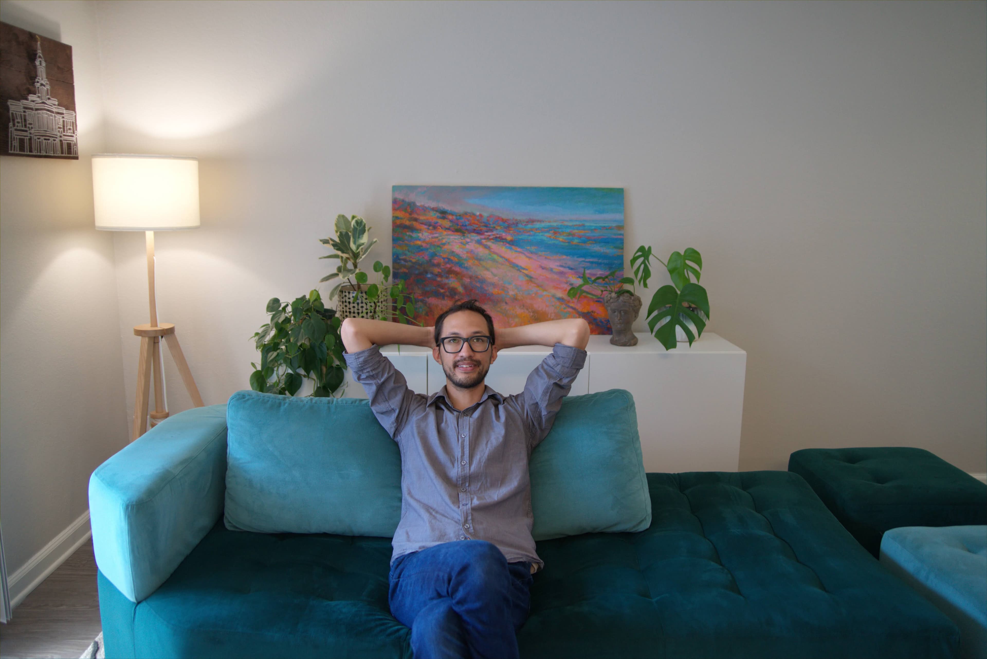 Daniel leaning back on a teal sofa with hands behind his head.